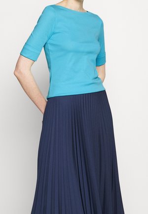 Turquoise fitted top with elbow sleeves paired with a pleated navy skirt, showcasing smooth texture and tailored silhouette.