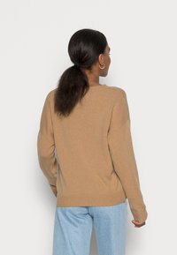 Beiger, gerippter Pullover mit lockerem Sitz, überschnittenen Schultern und langen Ärmeln. Kombiniert mit hellblauen Jeanshosen. Keine sichtbaren Logos oder Muster.