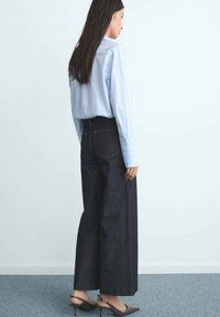 Breda ben mörka denimjeans kombinerat med en ljusblå randig skjorta. Outfiten har en avslappnad passform och minimal detaljering.