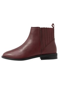 Bota de tobillo de cuero marrón liso con paneles laterales elásticos estriados, tira en la parte posterior y suela plana negra.