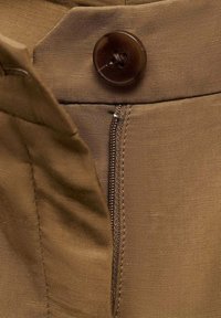 Un tissu brun avec une texture lisse présente un bouton rond et foncé ainsi une fermeture éclair visible le long de la couture latérale.