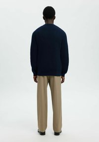 Jūras spēku zila ribota adīta džemperis ar garām piedurknēm, apaļu kaklu un brīvu piegriezumu. Apvienots ar gaiši bēšiem plašiem biksēm un melniem apaviem.