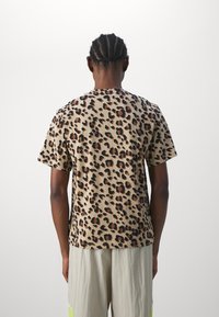 Krátký rukáv tričko s leopardím vzorem v béžové barvě s hnědými akcenty. Materiál vypadá měkký a střih je volný.