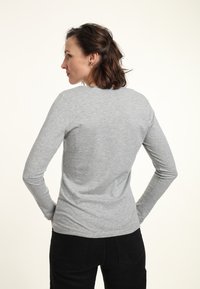 Graues Langarm-T-Shirt aus weicher Baumwolle, mit rundem Ausschnitt und körpernahem Schnitt, kombiniert mit schwarzen Hosen. Rückansicht gezeigt.