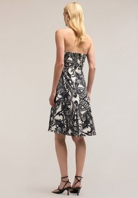 Rochie fără bretele, alb-negru, cu un corset mulat, tiv evazat, model complicat paisley și o textură fină. Pantofi cu toc subțire, negri.