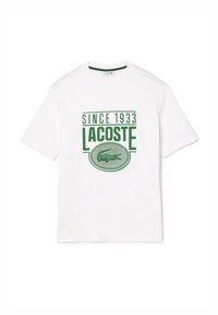 Camiseta de algodón blanca con un gráfico impreso en verde que muestra el texto "SINCE 1933" y "LACOSTE", junto con el logotipo de un cocodrilo. Cuello redondo.