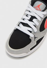 Γκρι και μαύρο αθλητικό παπούτσι με υφασμάτινο επάνω μέρος με υφή, λευκά κορδόνια, εμβληματικό λογότυπο και λείο λάστιχο σόλα με διακριτικές λεπτομέρειες.