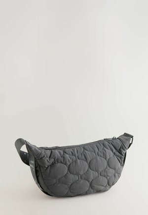 Õmmeldud must õlakott kõveriku kujuga, millel on lukuga sulgemine ja reljeefne muster tõstetud ringidega; reguleeritav rihm kaasas.