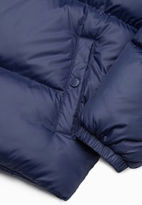 Marineblauwe gewatteerde jas met een gladde, glanzende textuur. Voorzien van een knoopaccent en elastische manchetten voor een aansluitende pasvorm. Toont doorgestikte vulling.