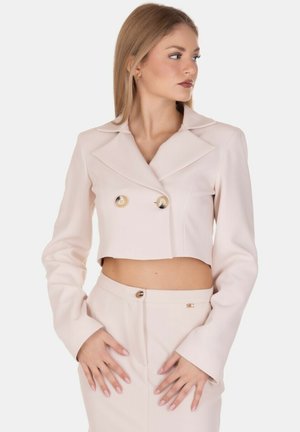 Blazer corto di un rosa tenue con un ampio colletto, design doppiopetto e bottoni dorati, abbinato a pantaloni coordinati e un sottile dettaglio del logo.