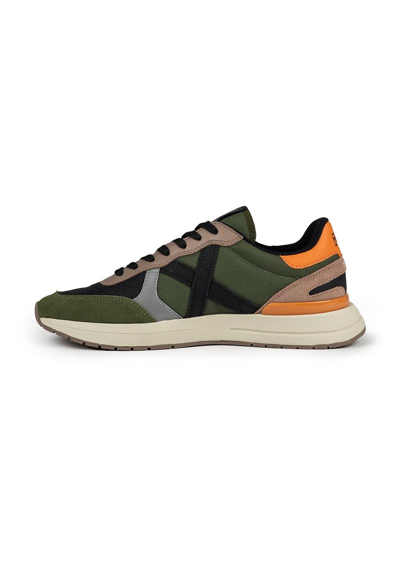 Zapatillas deportivas verdes y negras con una mezcla de materiales de ante y malla, que presentan detalles en beige y un talón naranja. Suela de goma suave.