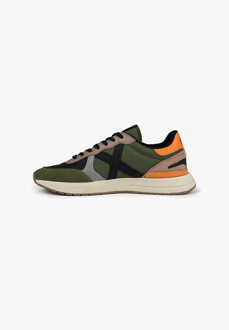Zapatillas deportivas verdes y negras con una mezcla de materiales de ante y malla, que presentan detalles en beige y un talón naranja. Suela de goma suave.