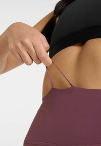 Fekete sportmelltartó állítható pántokkal, mely egy texturált, szilva színű sporttrikóra vált, mely illeszkedő kialakítással és varratmentes részletekkel rendelkezik.