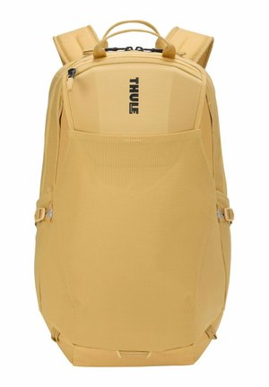 Zaino giallo Thule con spallacci imbottiti, maniglie superiori, tasca frontale in rete e tasca verticale con cerniera su sfondo bianco.