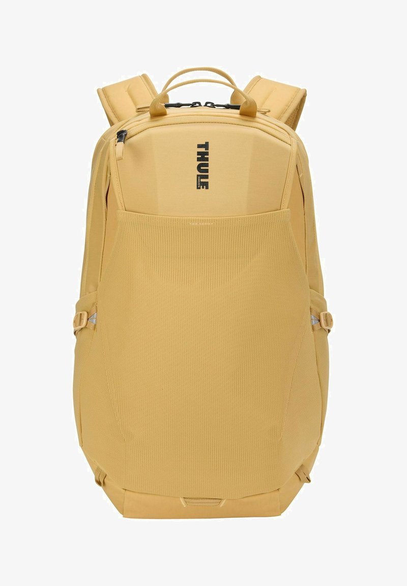 Sac à dos Thule jaune avec bretelles rembourrées, poignées supérieures, poche avant en mesh et poche verticale zippée sur fond blanc.