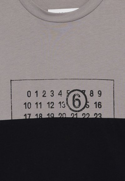 Kortärmad t-shirt med en grå överdel och svart underdel. Har ett tryck i kalenderstil i svart med ett framträdande cirkulerat nummer "6."