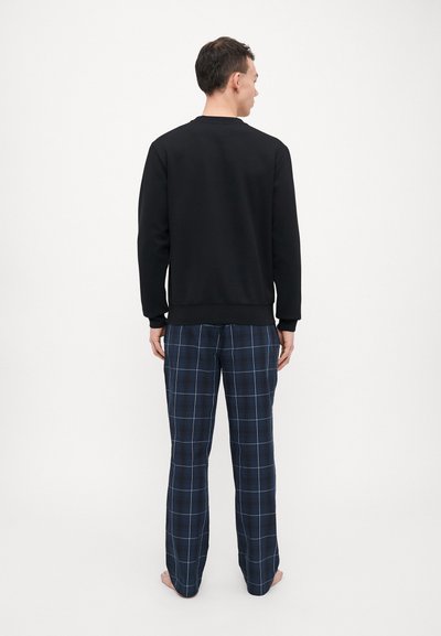 Sweatshirt noir avec poignets et ourlet côtelés, associé à un pantalon de pyjama  à carreaux marine avec un motif à carreaux bleu et blanc.