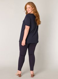 Donkerblauw kortaf T-shirt met zijsplitten, gecombineerd met paarse legging. Schoenen zijn gespsandalen met hakken, met een houten blokhak.
