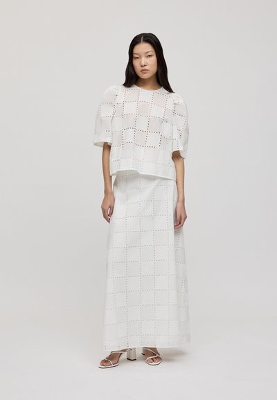 Ensemble blanc en deux pièces comprenant un haut à manches courtes et une jupe maxi, tous deux ornés de détails en découpes en forme de grille et d'une texture lisse.