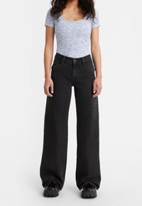 Ljusblå mönstrad kortärmad topp som matchas med svarta vida jeans med hög midja och en klassisk femficksdesign.