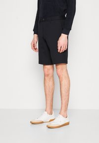 Sorte shorts laget av mykt stoff, med rett snitt, frontlommer og knappelukking, kombinert med hvite sneakers.
