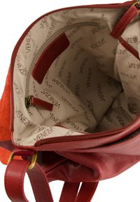 Rote Lederhandtasche mit Wildlederelementen. Futter aus Stoff mit Reißverschlussfach und dem Markennamen "Venezia" auf beigem Stoff gedruckt.