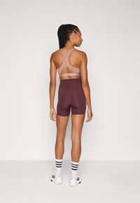 Brun sportbh med utskärningsdesign, bärs med matchande bruna shorts. Modellen har vita sneakers med svarta ränder och vita strumpor.