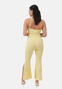 Mono amarillo de canalé con corpete ajustado, espalda descubierta y piernas acampanadas con aberturas laterales, combinado con sandalias blancas de tacón.