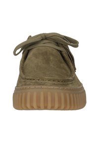 Vue de face d'une chaussure en daim vert olive avec une semelle épaisse en caoutchouc nervuré et des lacets noués sur un fond blanc uni.