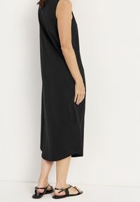 Svart ärmlös midiklänning i mjukt tyg med avslappnad passform och rundad nederkant. Matchas med svarta sandaler utan klack.