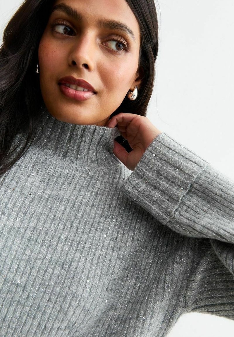 Maglione a collo alto grigio a coste con accenti di filo metallico. Presenta un collo alto e una vestibilità rilassata. Tessuto texturizzato con maniche lunghe.