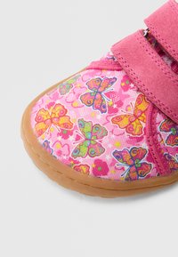 Pink fabric shoe with butterfly and flower patterns, featuring a velcro strap and a brown rubber sole.