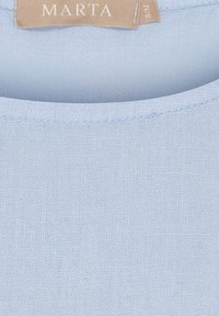 Lyseblå linnedragt med rund hals og struktureret overflade med et synligt mærke, der siger "MARTA." Glat stof med minimalt antal syninger.