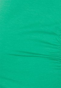Tecido verde com uma textura suave, apresentando variações subtis de tonalidade e ligeiros detalhes de pregas. Adequado para uso em vestuário.