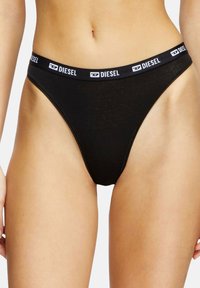 String noir fabriqué en tissu doux, doté d'une large ceinture élastique avec le logo "DIESEL". Ouvertures de jambes hautes pour une silhouette minimale.