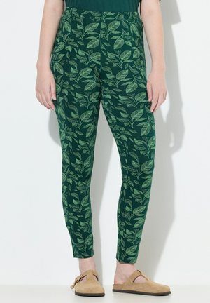 Green patterned leggings featuring a leafy design, made of soft fabric with a fitted shape. Paired with beige slip-on shoes.