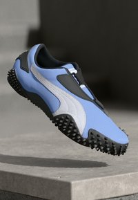 Lyseblå sportsko med syntetisk overdel, svarte og hvite detaljer, en strukturert såle med fremtredende knotter, og et strømlinjeformet design.