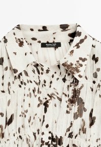 Chemise blanche à boutons avec un motif abstrait tacheté marron et noir et un col classique, arborant une étiquette Massimo Dutti.