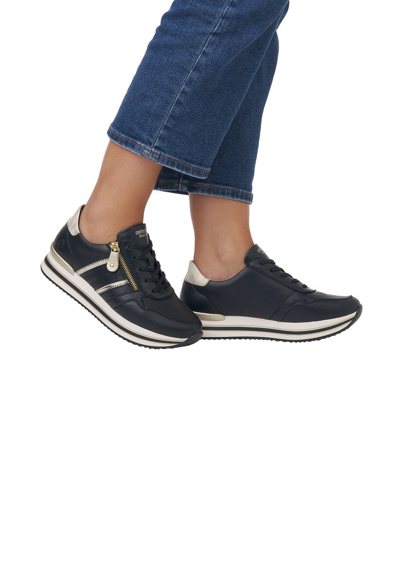 Sorte lædersneakers med guldlynlåse, en cremefarvet stribe på sålen og teksturerede detaljer på siderne.