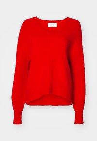 Pull en tricot rouge avec un col en V, des manches longues et une coupe décontractée. Tissu texturé et ourlet côtelé, avec une étiquette à l'intérieur du col.