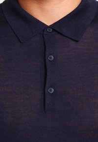 Polo bleu marine avec un col à revers, comportant trois boutons sombres et un tissu en maille texturée.