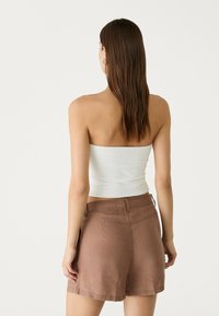 Top strapless bianco abbinato a pantaloni corti in lino marrone, con un tessuto testurizzato e una vestibilità rilassata. L'outfit ha un design minimalista.