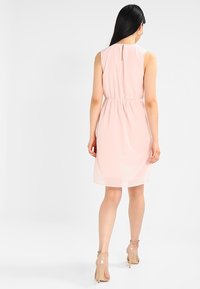 Ljusrosa ärmlös klänning med cinchad midja, detalj med nyckelhål i ryggen och en genomskinlig överdel, parat med sålta klackar.