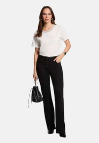 Top blanco de manga corta con cuello de cuentas y pantalones negros acampanados. Bolso negro con acentos estampados y zapatos negros.