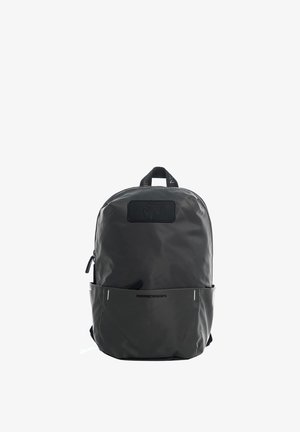Sac à dos noir minimaliste avec poche avant, poignée supérieure et fermeture éclair, arborant un petit patch logo et le texte "MAMM DESIGN" sur la poche.