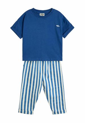 Camiseta de algodón azul con mangas enrolladas, que presenta un pequeño detalle de tiburón, combinada con pantalones de algodón a rayas en crema y azul.