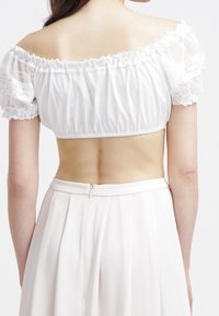 Donna che indossa un top corto bianco senza spalline con maniche in pizzo e una gonna bianca a vita alta, vista di spalle.