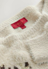 Beige gestrickter Pullover mit flauschiger Textur, versehen mit einem roten Etikett, auf dem "WEIHNACHTEN BEI NEXT" steht, und verziert mit dekorativen Elementen in Gold und Braun.