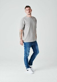 Sivá tričko s krátkymi rukávmi, spárované s modrými skinny džínami a bielymi teniskami s čiernym swoosh logom. Jednoduchý, neformálny dizajn.