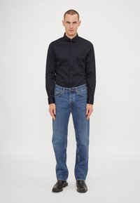 Camisa negra de botones, jeans de mezclilla azules y calzado negro. La camisa es elegante y los jeans son rectos con un acabado desgastado.